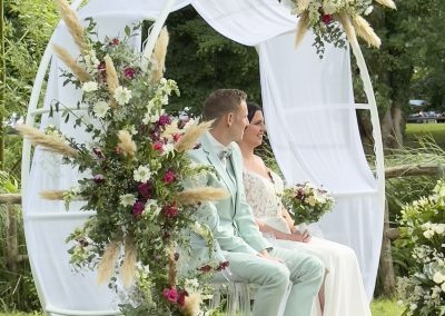 Cérémonie laïque sonorisée par Many Events, les mariés sont assis sous l'arche ronde et fleurie, écoutant les discours des invités.