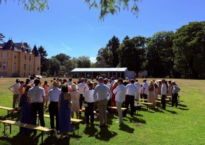 Les invités se tiennent debout dans l'herbe devant le château pour l'arrivée des mariés à la cérémonie laïque